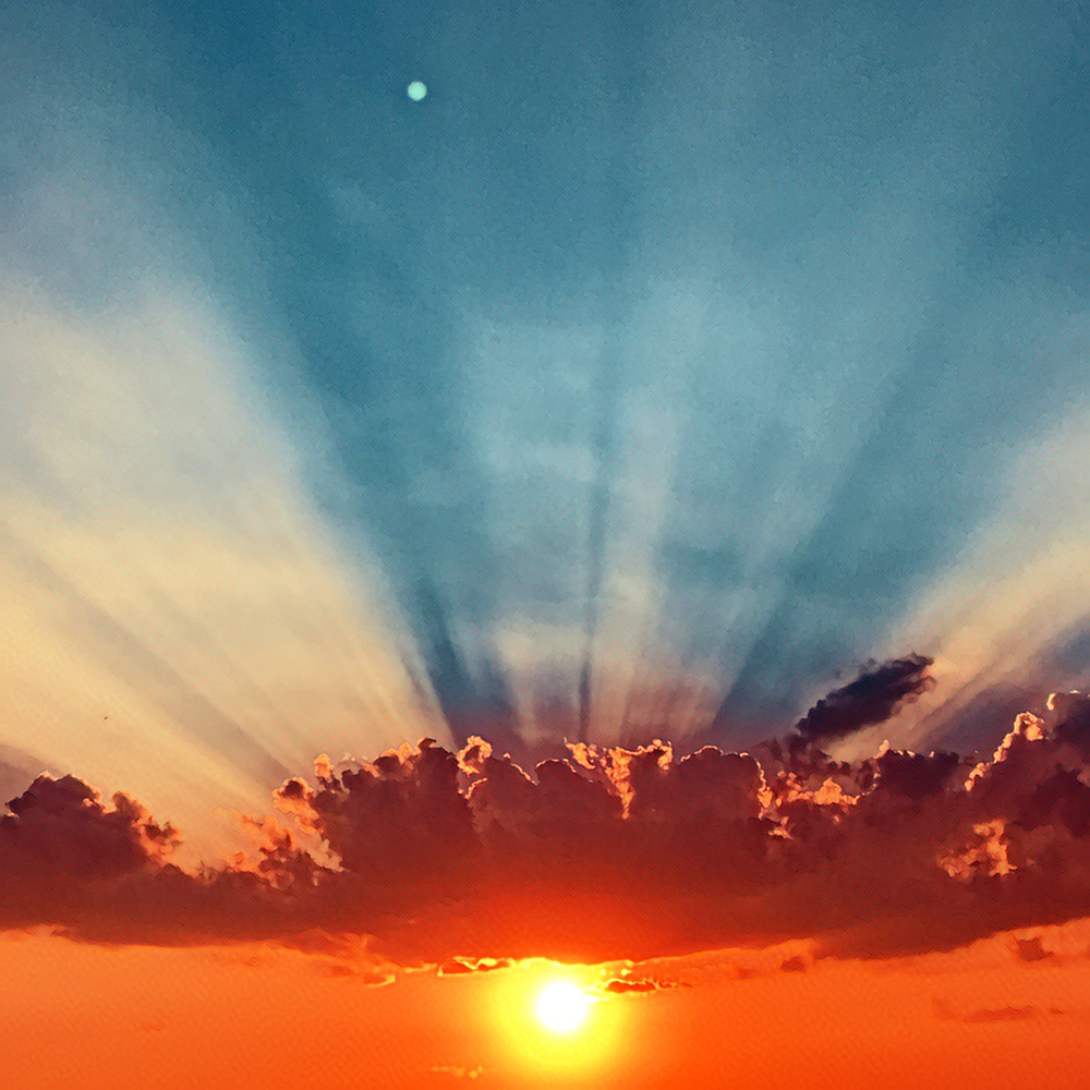 A solar horizon photograph in which the direction of the sun's transition is indistinguishable. Sun at threshold, rays fanning upward into a teal-blue sky. Neither clearly dawn nor dusk.
